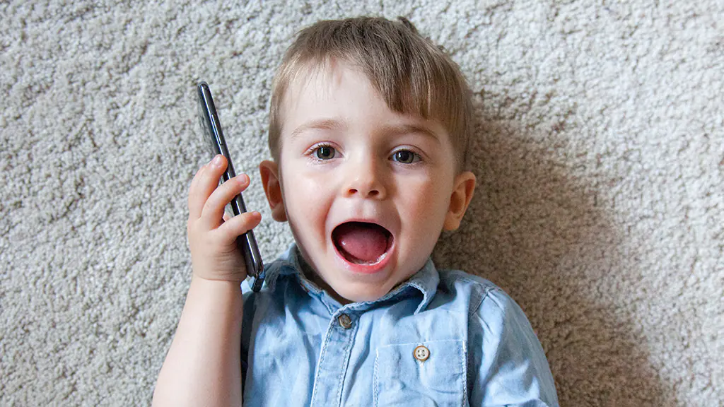 A child looks surprised while holding a smartphone close to his ear.