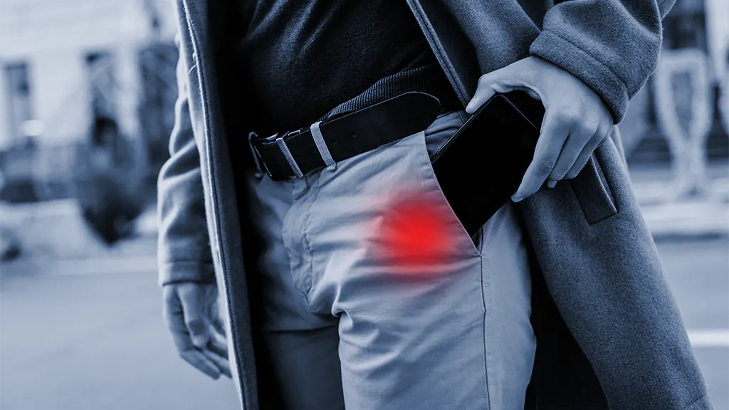 A man is holding a smartphone, popping out of his pocket. Around the phone, there is red glowing implying phone radiation.