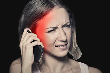 A woman talking on the phone. Around her ears, a red color effect shows the spread of radiation.  Her face has a slight pained expression.