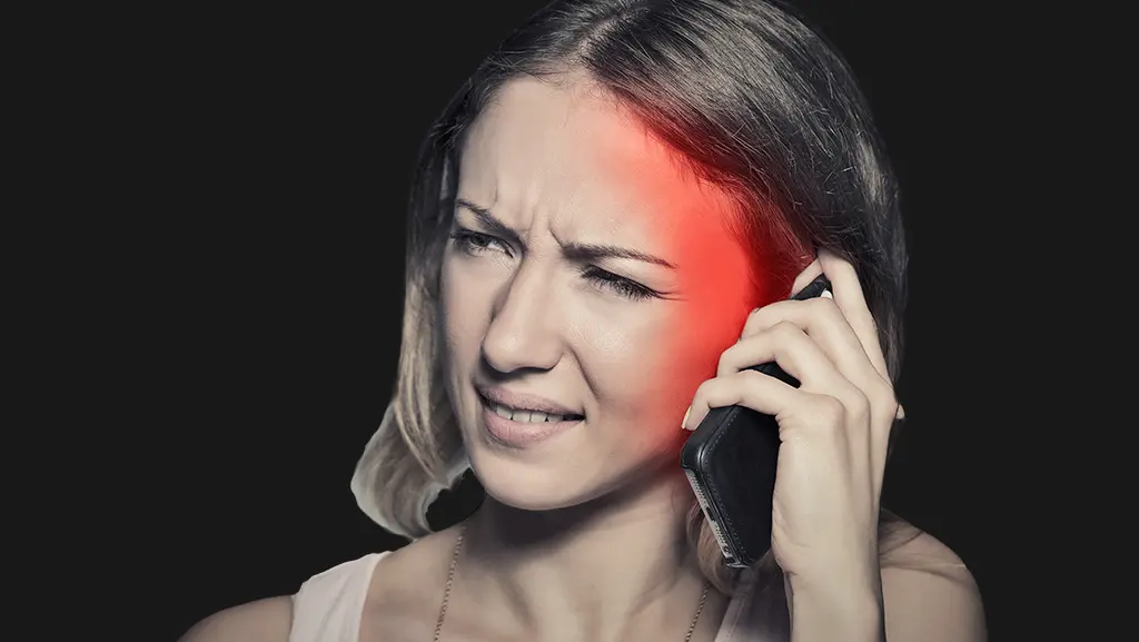 A woman talking on the phone. Around her ears, a red color effect shows the spread of radiation.  Her face has a slight pained expression.